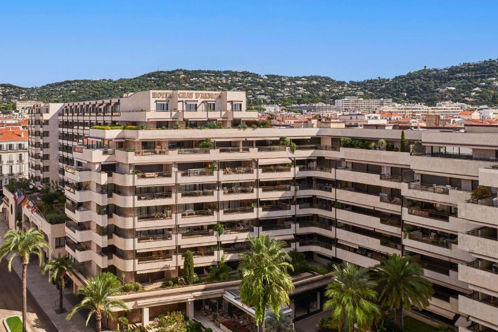 an apartment building with palm trees in front of a city at Hôtel Barrière Le Gray d'Albion in Cannes