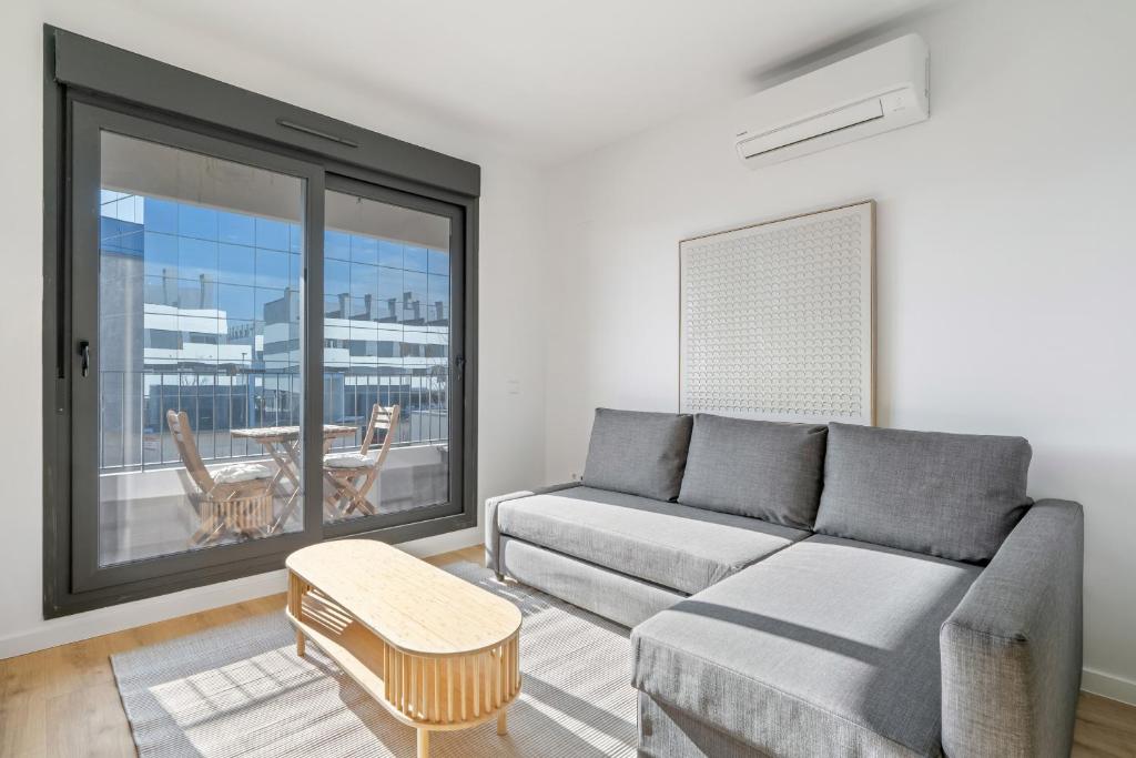 ein Wohnzimmer mit Couch und großem Fenster in der Unterkunft apartamentos con piscina de invierno y garaje ALQUILER TEMPORAL in San Sebastián de los Reyes