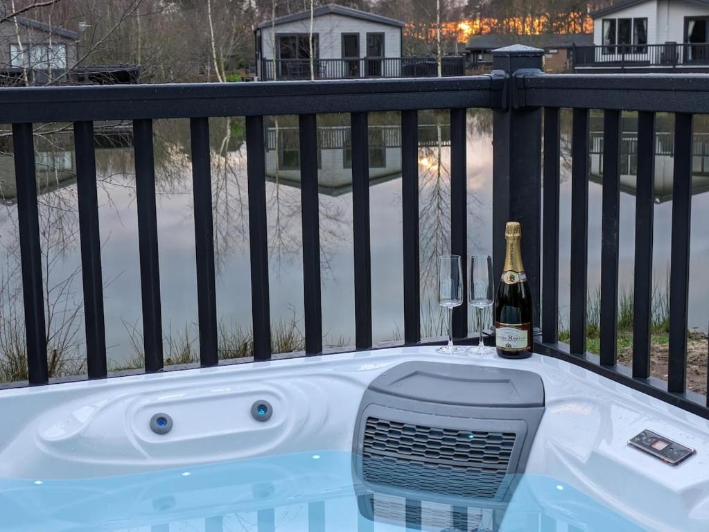 ein Whirlpool auf einem Balkon mit einer Flasche Champagner in der Unterkunft Kingfisher Lodge - Lakeside Lodge With Hot Tub in Woodhall Spa