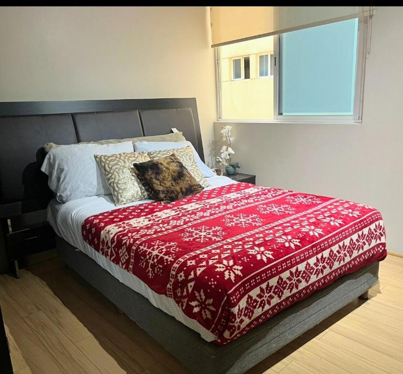 un letto con una coperta rossa e una finestra di Acogedora Recamara Matrimonial con Blackout - A solo 2 cuadras del WTC! a Città del Messico