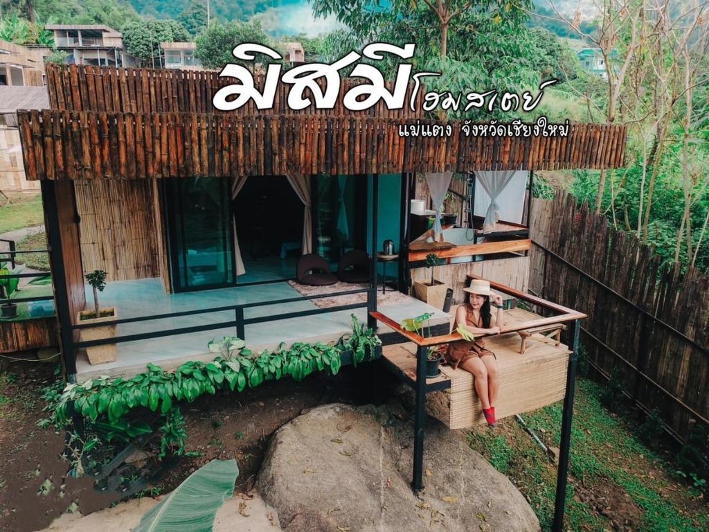 a woman sitting on a bench in front of a house at Missme Homestay-มิสมีโฮมสเตย์ in Ban Mae Na