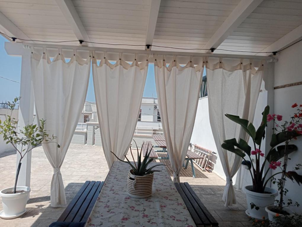 a patio with white curtains and a table with potted plants at Le Perle in Maruggio