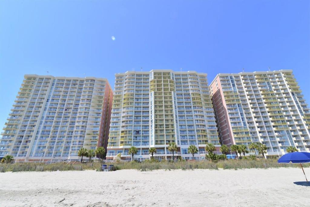 two tall buildings on the beach with an umbrella at Oceanfront TOP LOCATION MODERN RESORT Lazy River Huge Pool Oasis in Myrtle Beach