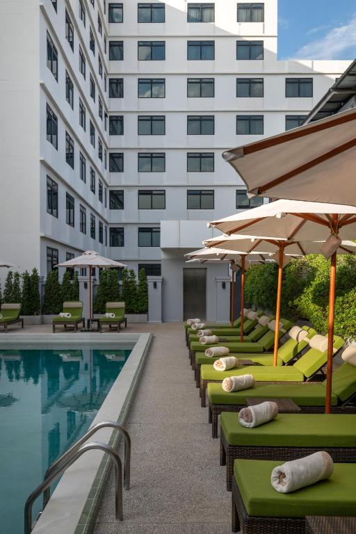 a row of lounge chairs with umbrellas next to a swimming pool at Dusit Princess Chiang Mai in Chiang Mai