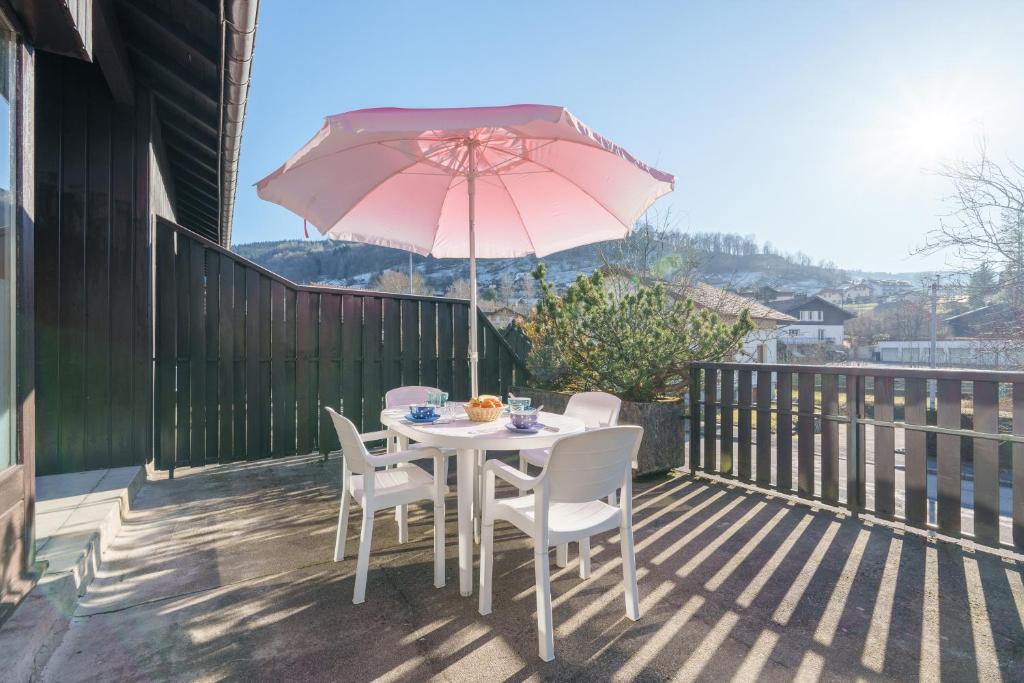 a table and chairs with a pink umbrella on a deck at Le Refuge des Cerfs - Duplex vue montagne in La Bresse