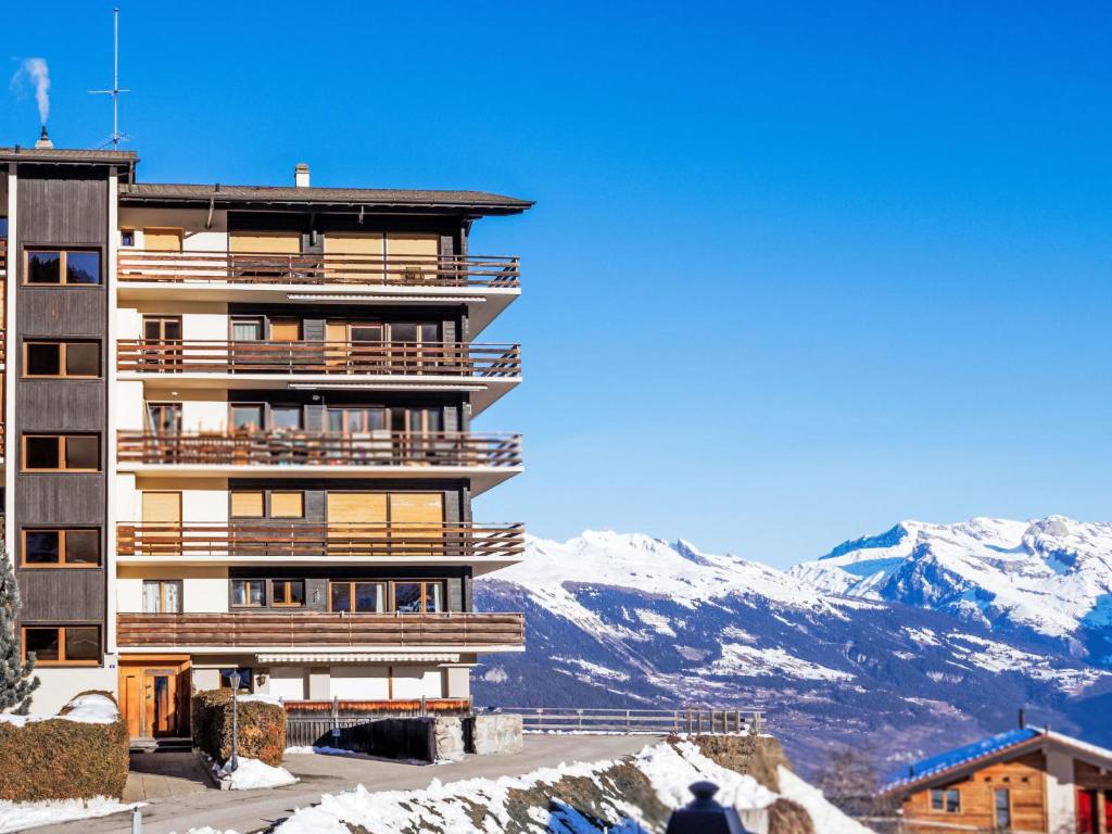 um edifício alto com montanhas cobertas de neve ao fundo em Apartment Les Arolles A1 by Interhome em Nendaz