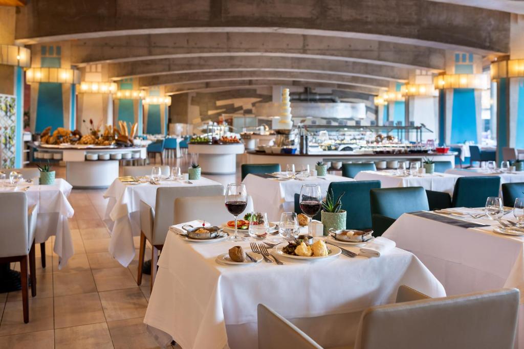 a restaurant with white tables and chairs and a kitchen at MUR Faro Jandia Fuerteventura & Spa in Morro del Jable