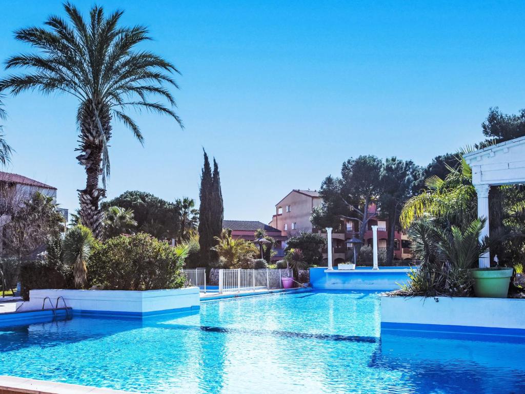 une grande piscine avec des palmiers et des bâtiments dans l'établissement Apartment Malibu Village by Interhome, à Canet