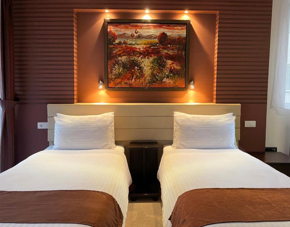 two beds in a hotel room with a painting on the wall at Sienna Apartments in Skopje