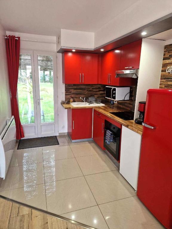 Il comprend une cuisine équipée de placards rouges et d'un réfrigérateur rouge. dans l'établissement 02 - Très joli 2 pièces avec 3 lits pouvant accueillir jusqu'à 5 personnes, situé au rdc avec entrée indépendante, une place de parking réservée devant l'entrée et terrasse sur l'arrière donnant sur parc arboré, tout le linge de maison est fourni, à Razac-sur-lʼIsle