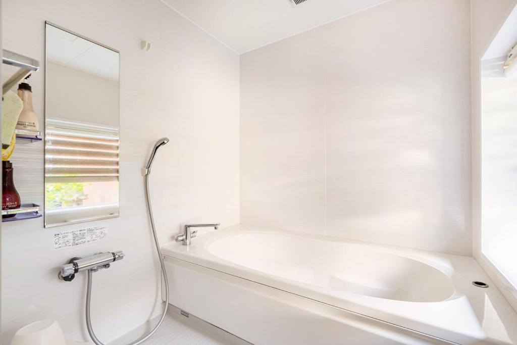 a white bathroom with a tub and a mirror at Manabi-stay Matsue 駅近伊勢宮町どこに行くにも最高に便利な古民家一棟貸切ホテル in Matsue