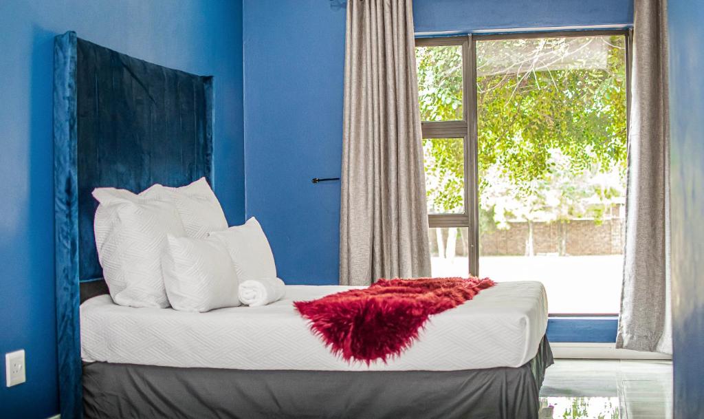 a blue bedroom with a bed with a red blanket on it at Koeneng B&B in Kempton Park