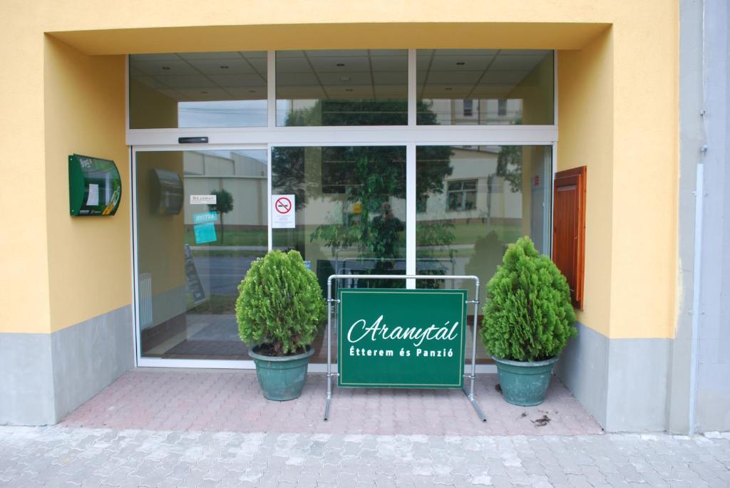 a sign in front of a store with two plants at Aranytál Panzió in Komárom