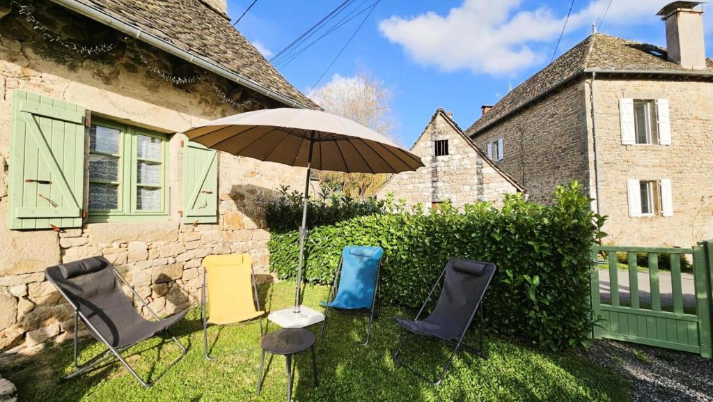 a group of chairs and an umbrella in front of a house at Gîte de France à Darazac 2 épis - Gîte de France 2 personnes MAE-5181 in Darazac