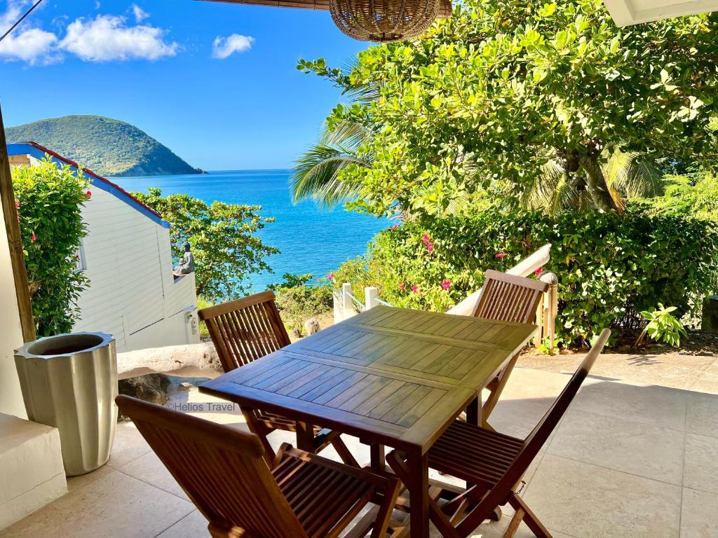 a wooden table and chairs on a patio with the ocean at Cottage Honoré Paradise in Deshaies