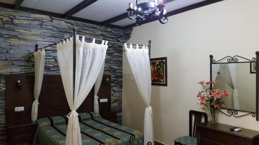 a bedroom with a bed with curtains and a stone wall at Hostal Restaurante El Lirio in Bollullos par del Condado