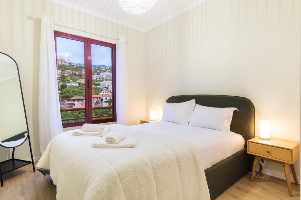 a white bedroom with a large bed with a window at GuestReady - Charming home in Câmara de Lobos in Câmara de Lobos