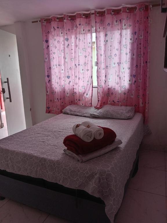 a bed with two towels and a window with pink curtains at Pousada Vicenzi in Luziânia
