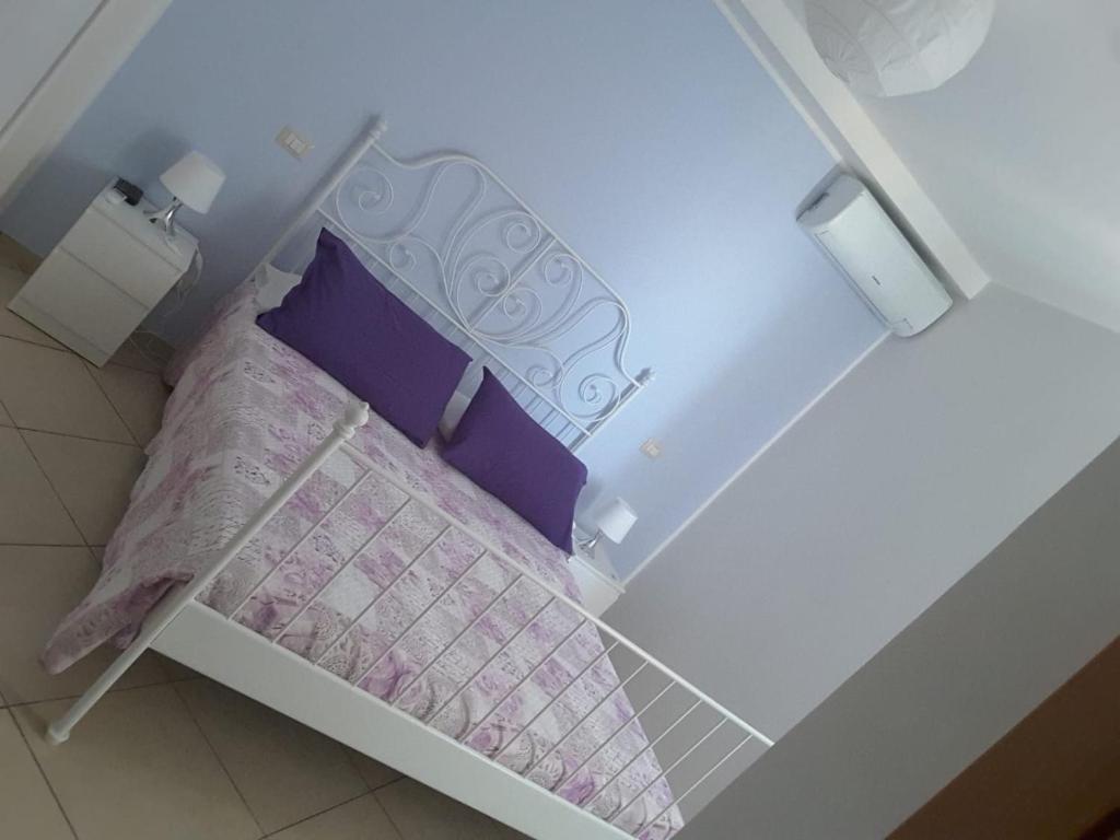 un piccolo letto con lenzuola e cuscini viola e bianchi di Iriss a Taormina