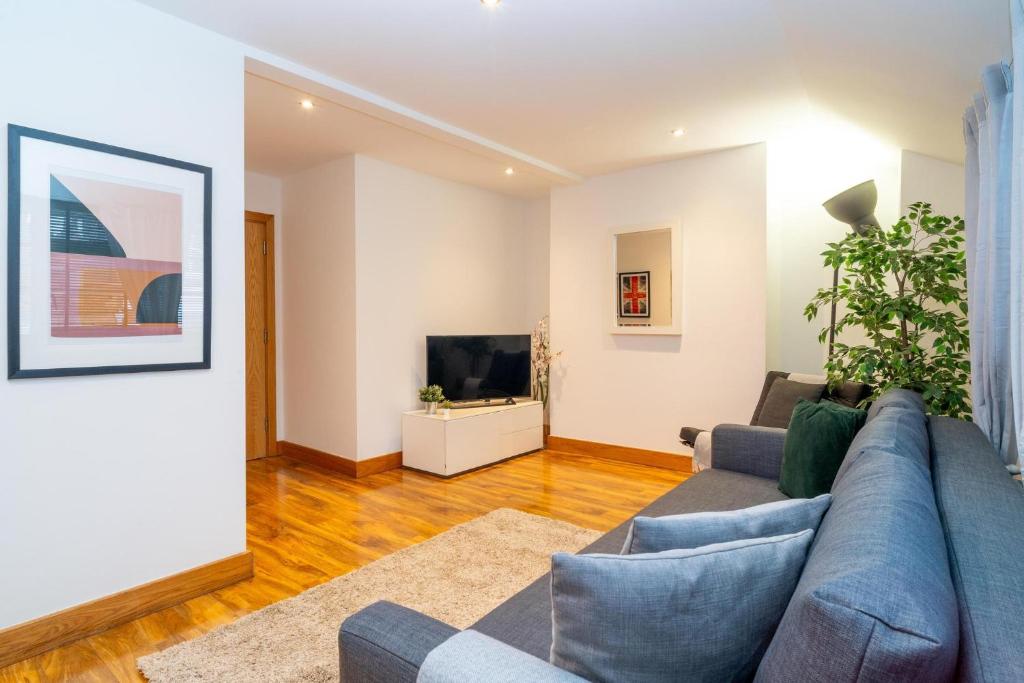 a living room with a blue couch and a tv at Cuthbert Suite - Heart of Covent Garden! in London