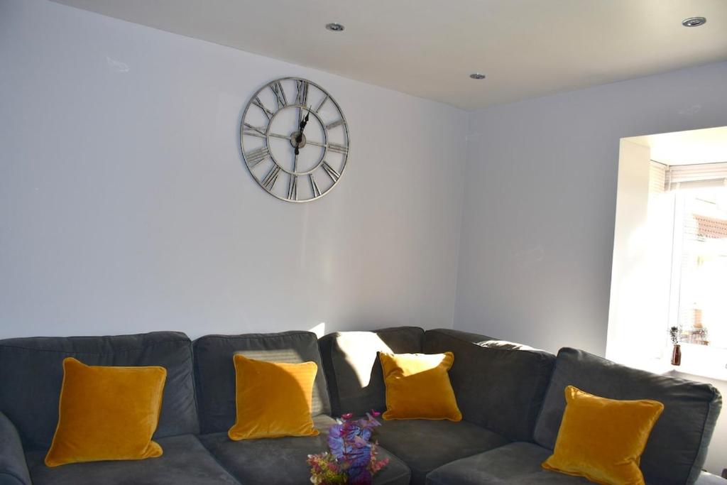 a black couch with yellow pillows in a living room with a clock at 2 Bedroom semi-detached house Luton in Luton
