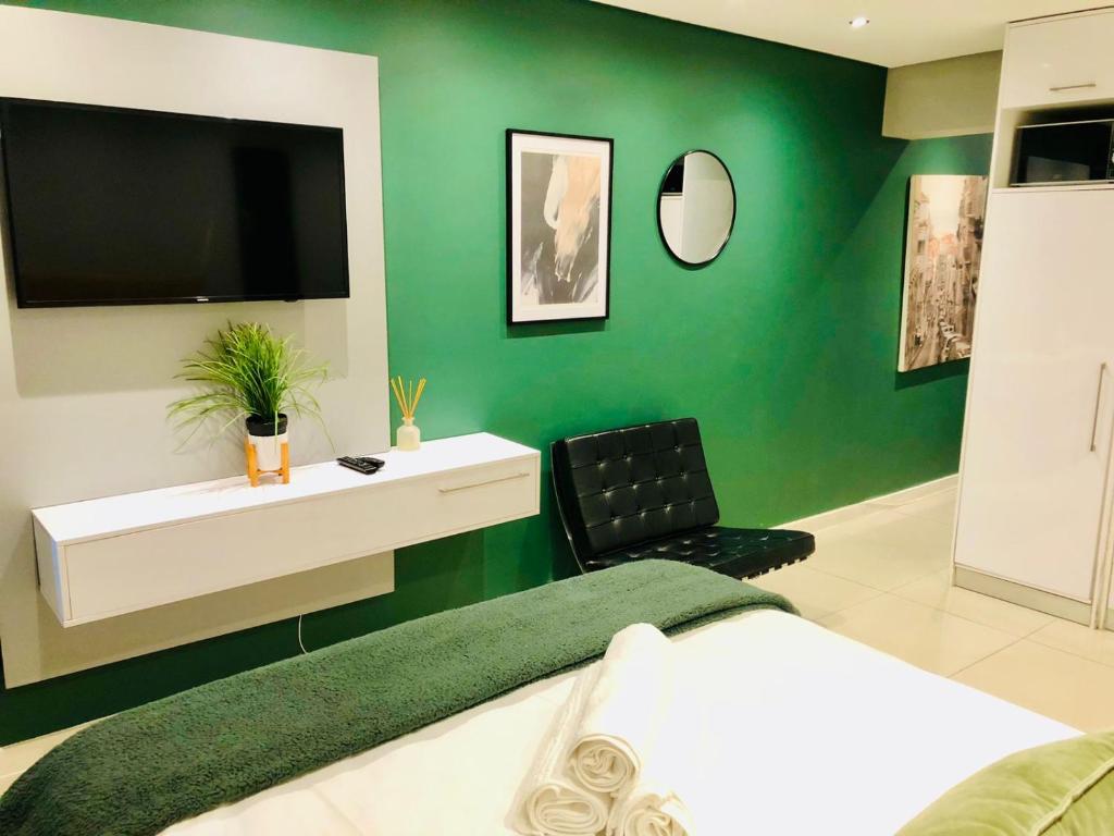 1 dormitorio con una pared verde, 1 cama y TV en Modern Apartment in Mouille Point with Green Point Park Access, en Ciudad del Cabo