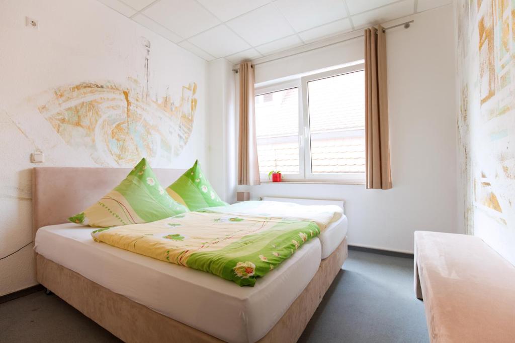 Schlafzimmer mit einem Bett mit grüner Bettwäsche und einem Fenster in der Unterkunft Hostel Jena in Jena