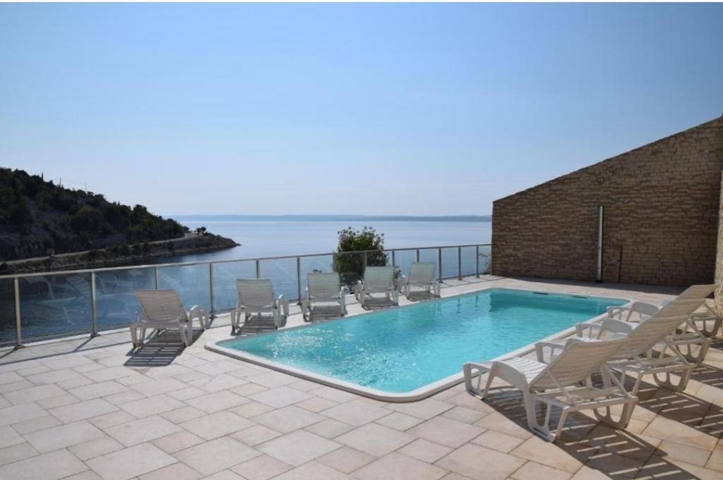 a swimming pool with chairs and the ocean in the background at Apartments & Rooms Jure in Viniština