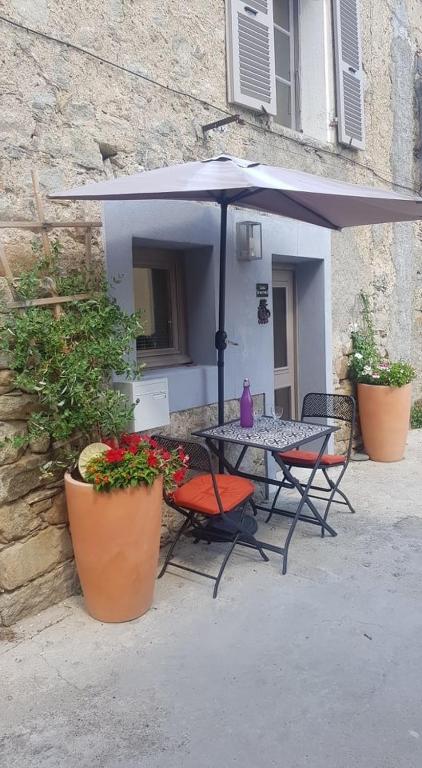 une table et des chaises sous un parasol devant un bâtiment dans l'établissement 10 min de Cortè, 5 couchages,, à Venaco