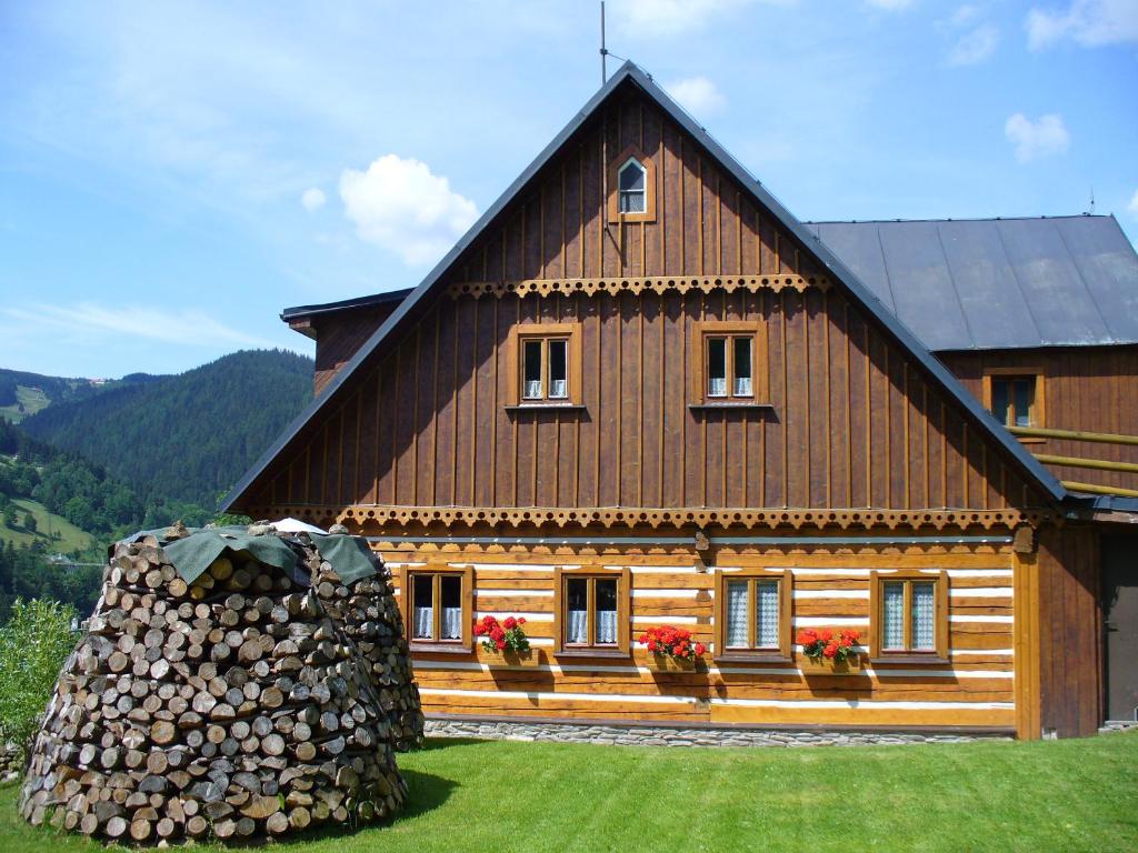 a large wooden house with a pile of logs in front of it at Bouda Na Cestě in Pec pod Sněžkou