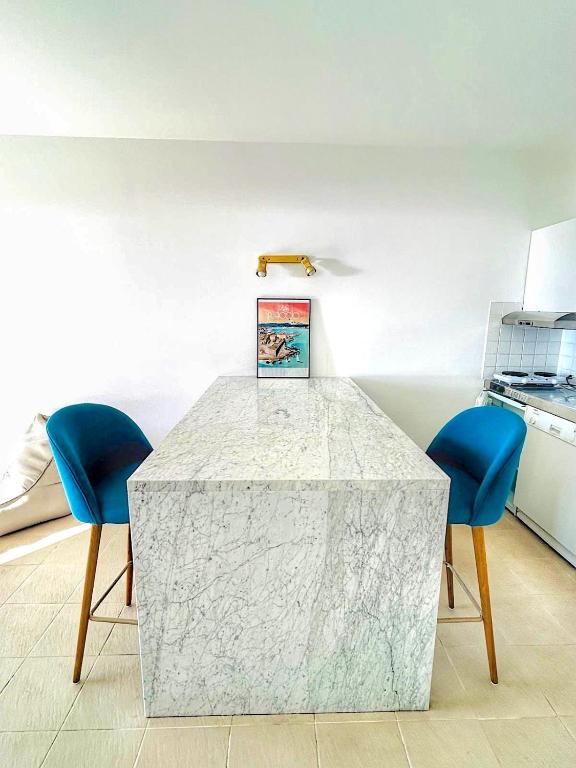 - une cuisine avec une table en marbre et deux chaises bleues dans l'établissement Studio - ARIA MARINA - Route des sanguinaires - plage à 30m - Parking gratuit - Terrasse - Emplacement idéal, à Ajaccio