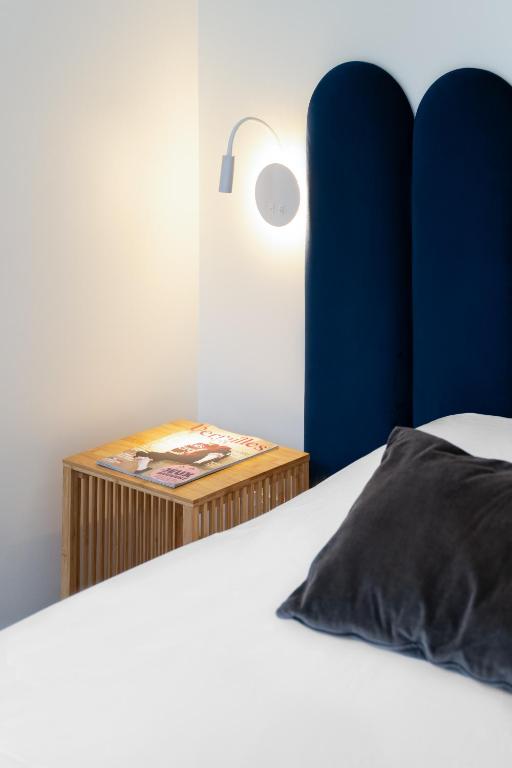 a bed with a blue headboard and a table with a lamp at Hôtel d'Angleterre in Versailles