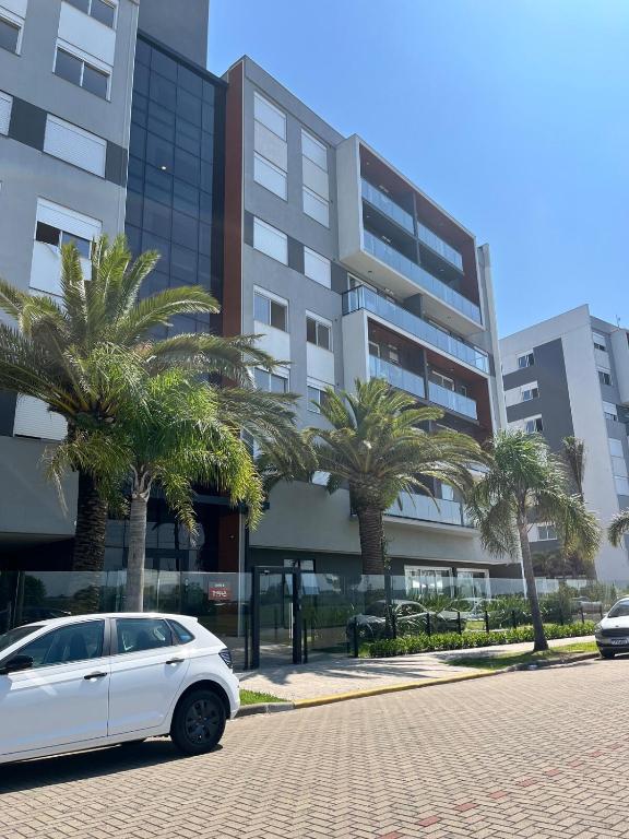 a white car parked in front of a building with palm trees at Apartamento alto padrão in Xangri-lá