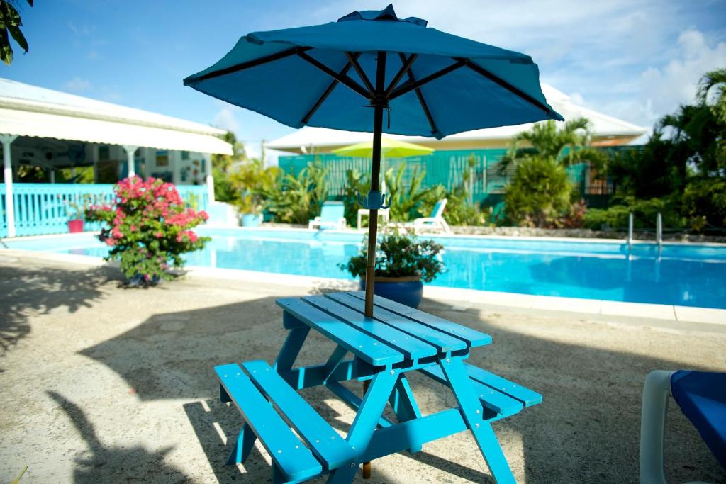 a blue picnic table with an umbrella next to a pool at Hotel Cap Sud Caraibes in Le Gosier