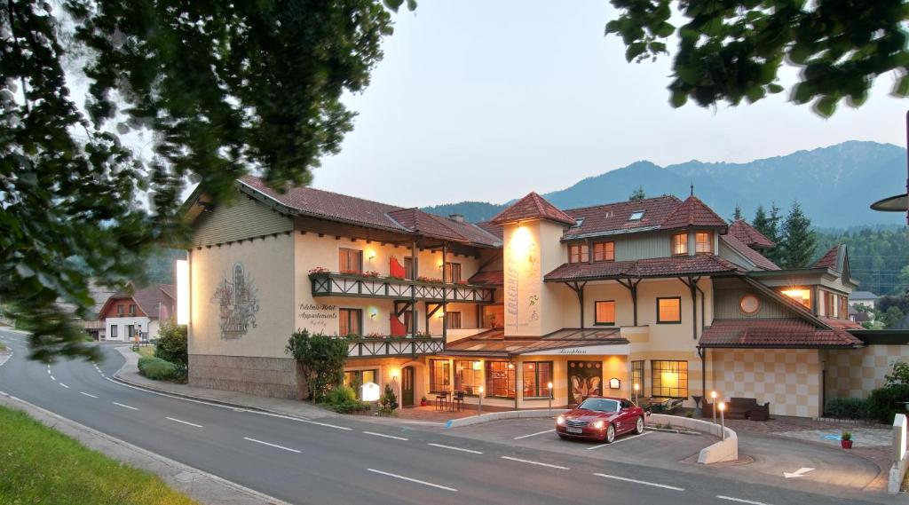 un gran edificio con un coche aparcado delante de él en Erlebnis-Hotel-Appartements, en Latschach ober dem Faakersee