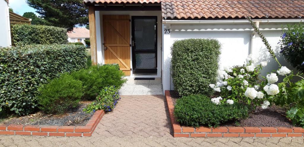 une porte d'entrée d'une maison avec des buissons et des fleurs dans l'établissement Maison dans résidence avec piscine et tennis - 4 personnes, à Pornic
