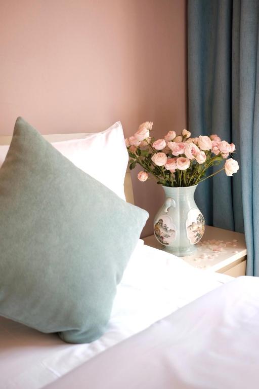 a vase of pink flowers on a bed with a pillow at 福来小院民宿 in Jiezi Ancient Town