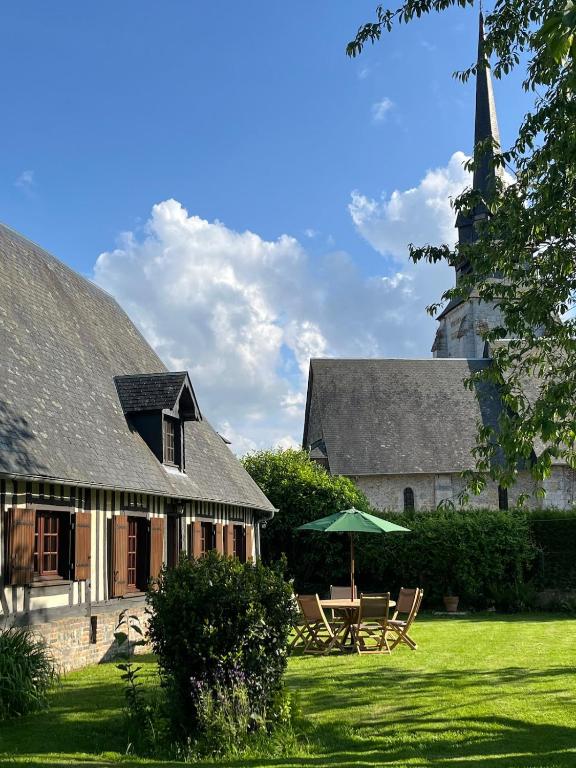 une maison avec des chaises, un parasol et une église dans l'établissement La Grange, la Lande St Leger, à La Lande