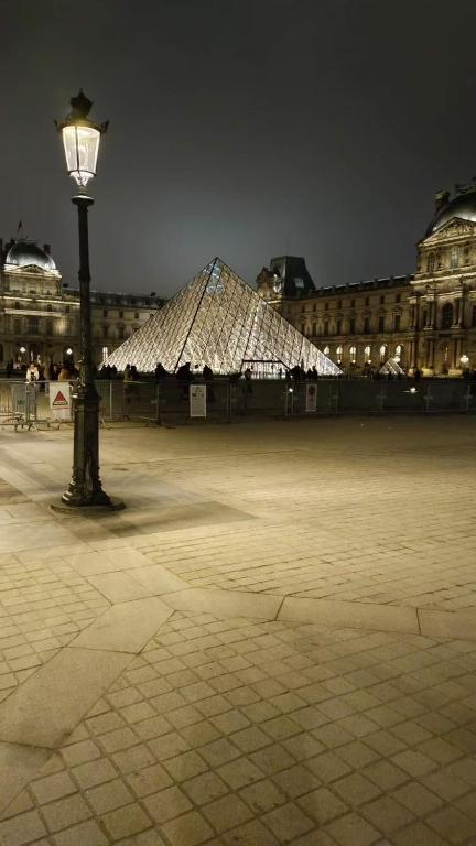 un pôle lumineux et un bâtiment avec une pyramide dans l'établissement cosy appartement next to Louvre, à Paris