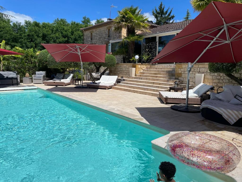 a swimming pool with red umbrellas next to a house at Chambre d hôte grise avec petit déjeuner Sauna et Piscine inclus Jacuzzi en option in Sarlat-la-Canéda