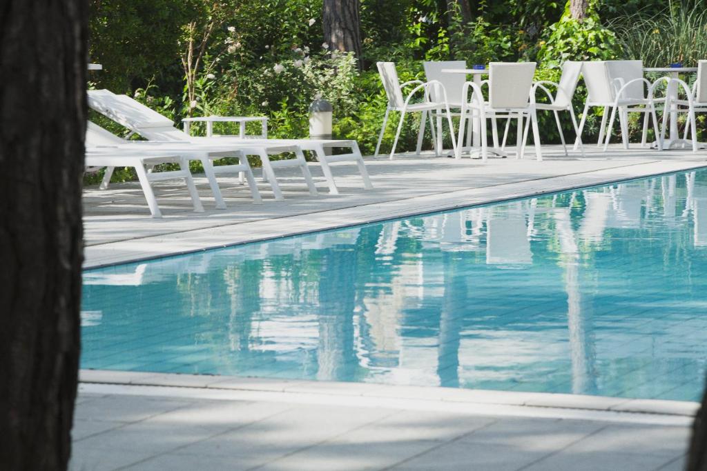 un grupo de sillas blancas sentadas junto a una piscina en Hotel Caracas en Lignano Sabbiadoro