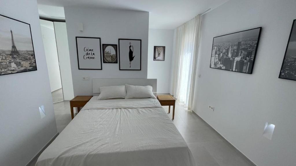 een witte kamer met een bed en foto's aan de muur bij apartament in Marbella