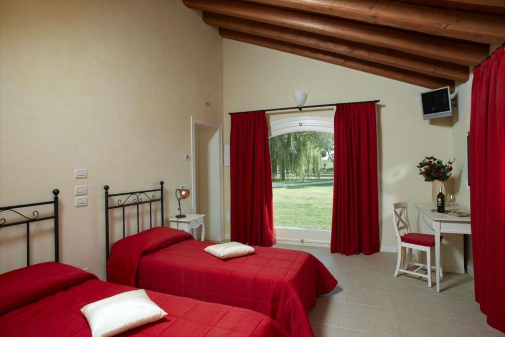 two beds in a bedroom with red sheets and a window at Tenuta Santomè in Biancade