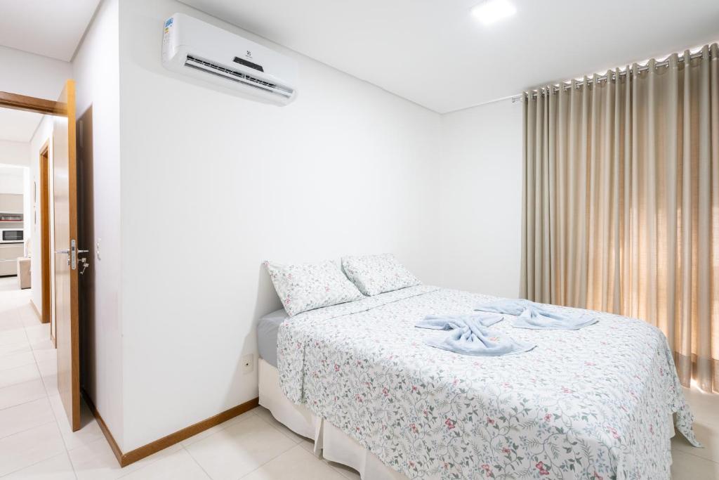 a white bedroom with a bed and a window at Apto Vista Mar Home Club Pé na Areia 3 Quartos Ares Condicionados Cozinha Completa Piscina Aquecida Jacuzzi Sauna Academia Quadra Playground Salão de Jogos 15min do Beto Carrero in Piçarras