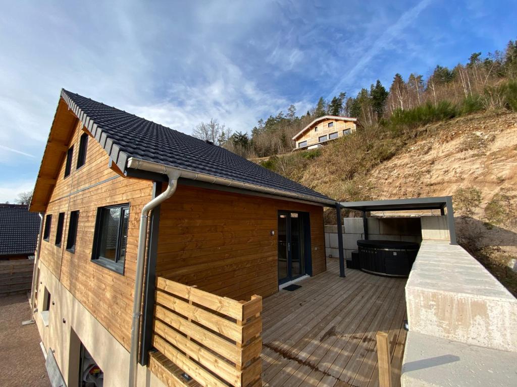 a house with a wooden deck next to a hill at Chalet muguet & Jaccuzi privatif in Rochesson