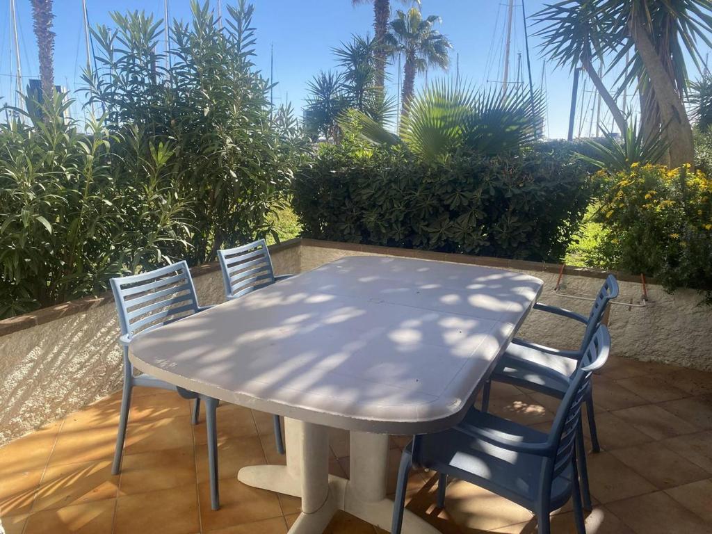 une table et des chaises blanches sur une terrasse avec des palmiers dans l'établissement Appartement rénové 2 pièces proche plage, 4 pers, parking privé - FR-1-782-74, au Barcarès