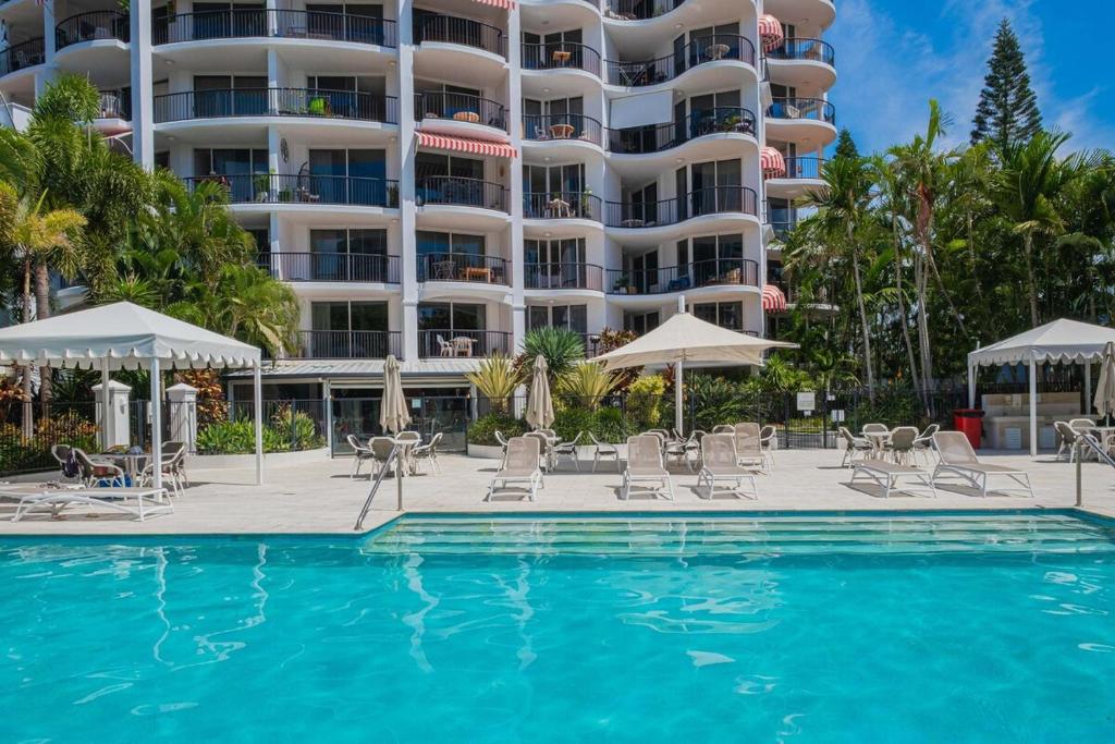 a swimming pool with chairs and umbrellas in front of a hotel at 1BR Tropical Escape with Heated Pools Sauna BBQ in Gold Coast