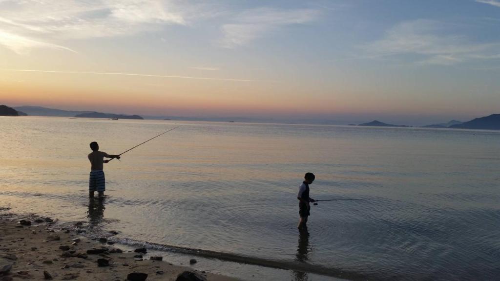 two men standing in the water fishing on the beach at Fun stay大島 の1棟貸し宿 in Suo Oshima