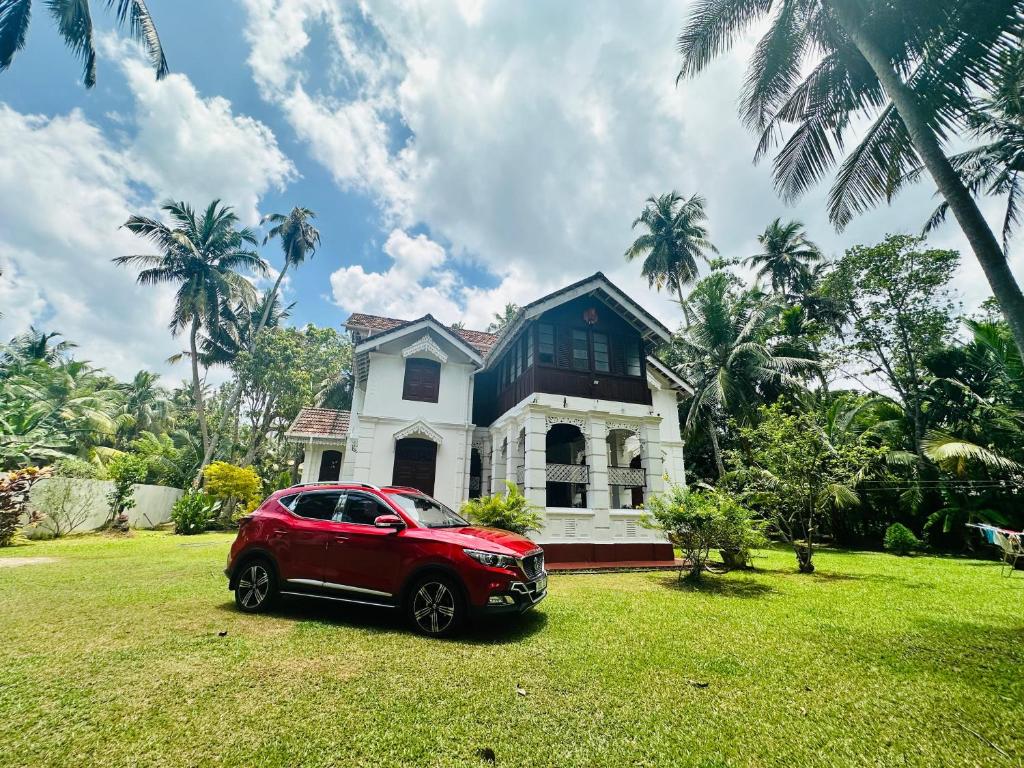 a red car parked in front of a house at Charlotte's Coral Breeze - A Colonial Seaside Bungalow in Hikkaduwa