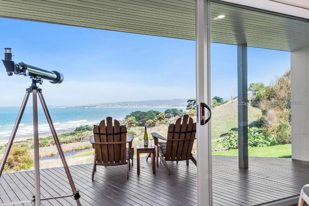 a camera and two chairs on a deck with a view of the ocean at Seafarers Getaway in Apollo Bay
